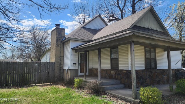view of front of home featuring covered porch, a shingled roof, fence, and a chimney