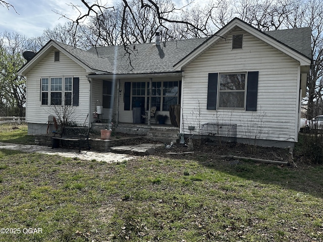 back of property with a lawn, covered porch, and roof with shingles