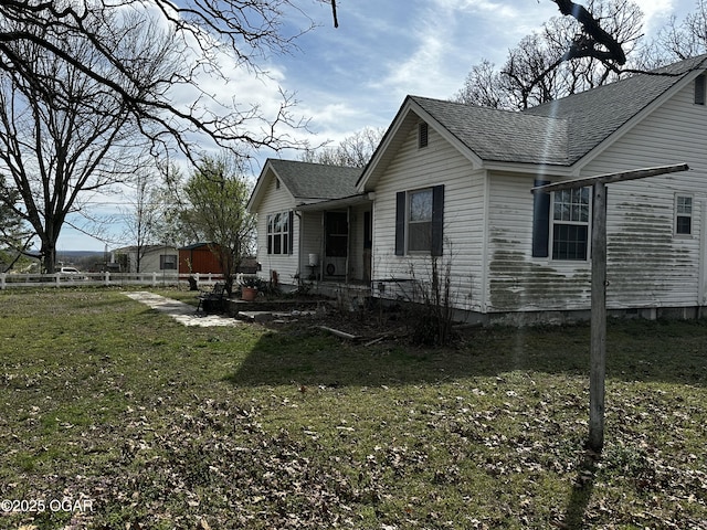 view of side of property with a shingled roof, fence, and a yard