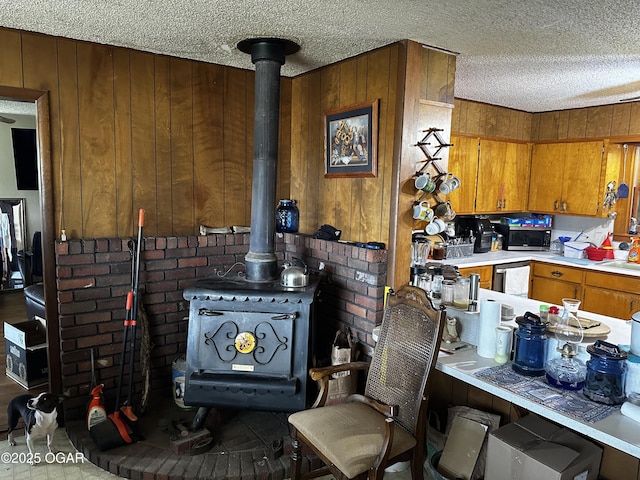 kitchen with light countertops, wood walls, a wood stove, a textured ceiling, and brown cabinets