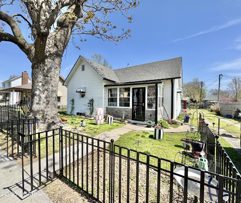 view of front of house with roof with shingles, a front lawn, stone siding, and a fenced front yard
