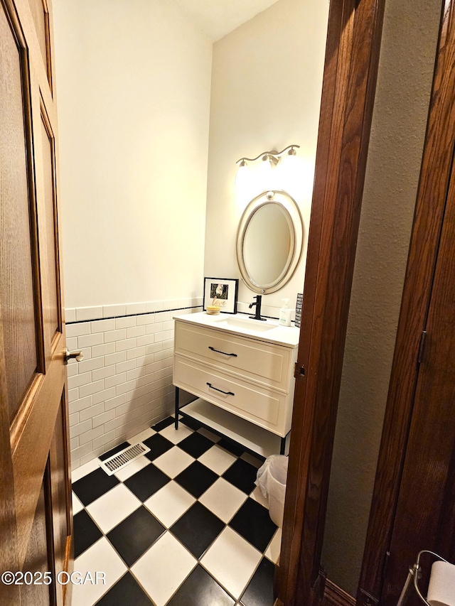 half bathroom featuring visible vents, a wainscoted wall, vanity, and tile walls