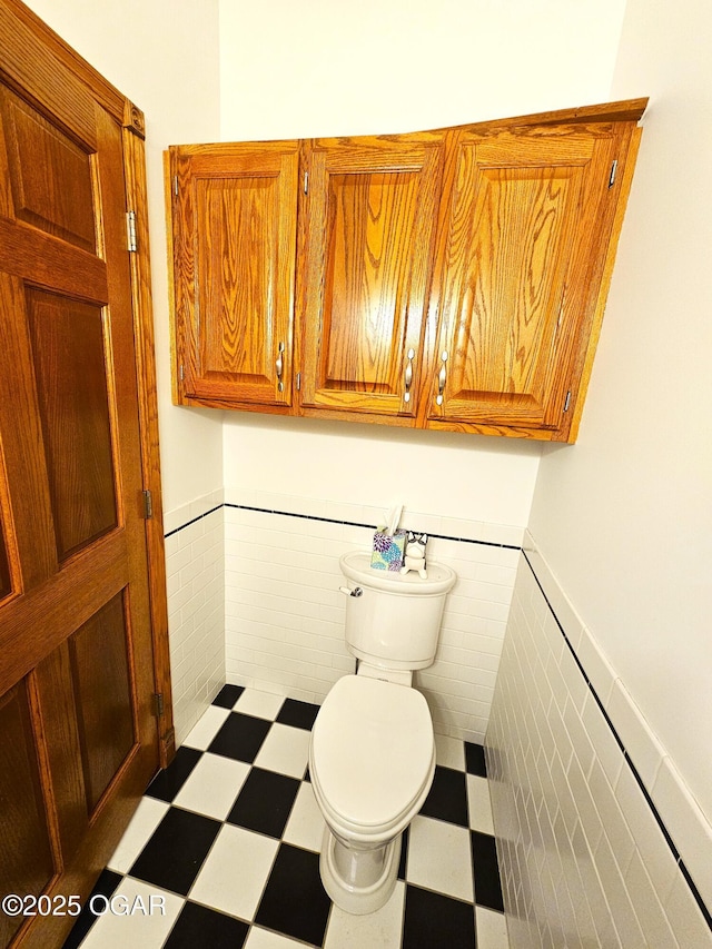half bathroom featuring toilet, tile walls, tile patterned floors, and a wainscoted wall