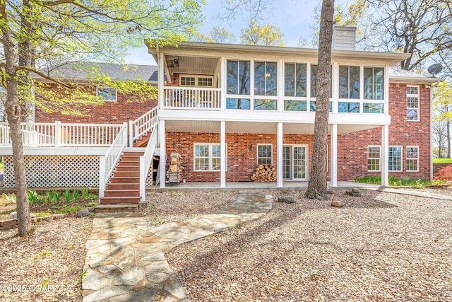 rear view of house with a chimney, stairs, brick siding, a patio area, and a sunroom