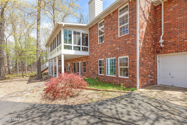 view of home's exterior featuring brick siding, a chimney, a sunroom, and concrete driveway