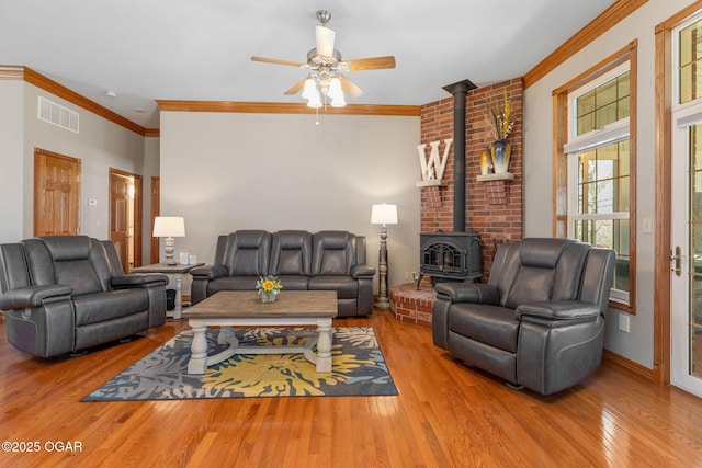 living area with ornamental molding, visible vents, a wood stove, and wood finished floors