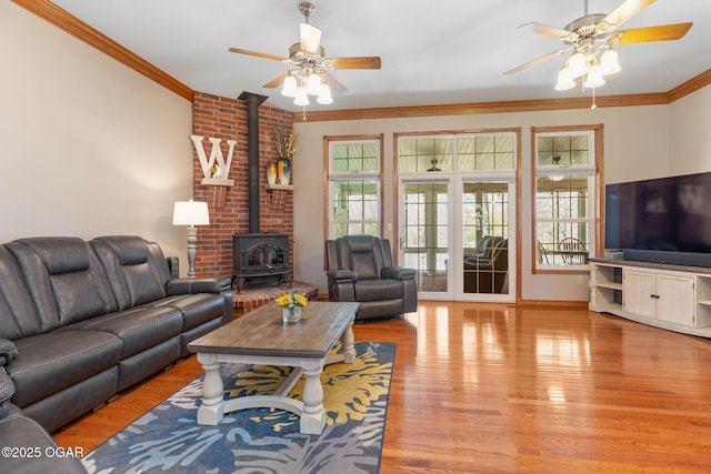 living room with a wood stove, light wood-type flooring, ornamental molding, and ceiling fan