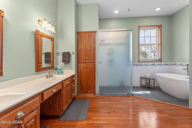 bathroom with a freestanding bath, a sink, a shower stall, wainscoting, and wood finished floors