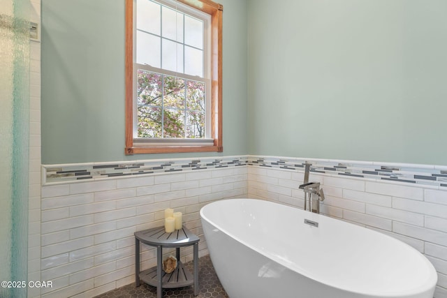bathroom featuring tile walls, a freestanding bath, and a wainscoted wall