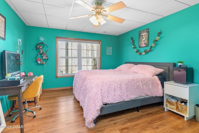 bedroom with baseboards, a ceiling fan, a paneled ceiling, and wood finished floors