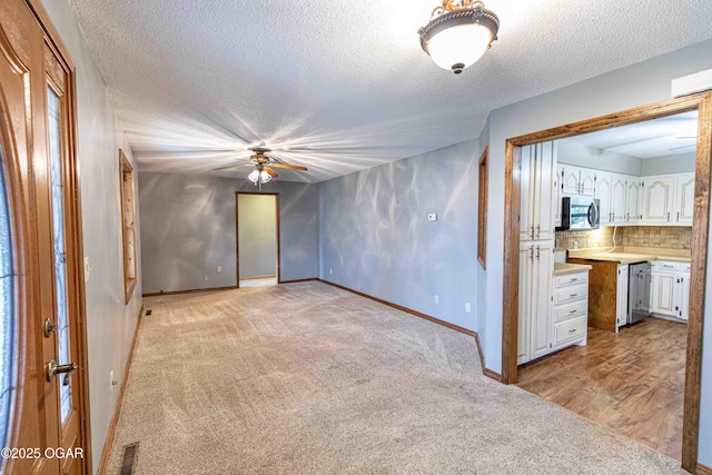 spare room featuring light carpet, a textured ceiling, baseboards, visible vents, and ceiling fan