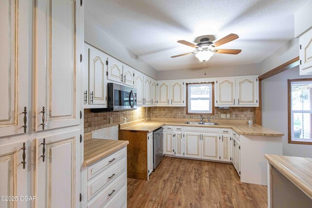 kitchen featuring light countertops, light wood-type flooring, backsplash, a sink, and appliances with stainless steel finishes