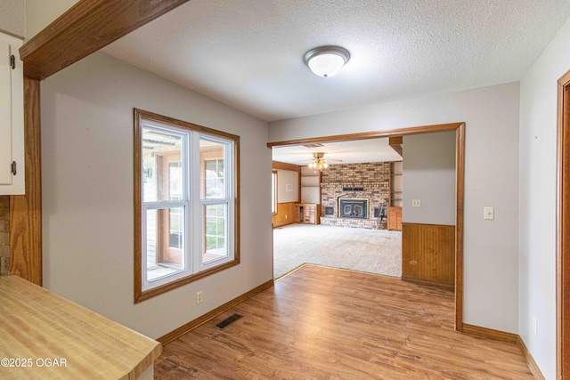 living room with a textured ceiling, wooden walls, a brick fireplace, ceiling fan, and light wood-style floors