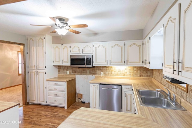 kitchen with decorative backsplash, ceiling fan, appliances with stainless steel finishes, a sink, and light wood-style floors