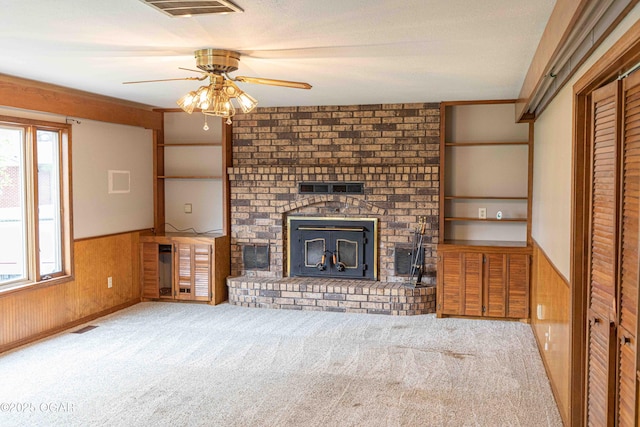 unfurnished living room featuring wood walls, a fireplace, a ceiling fan, carpet floors, and wainscoting