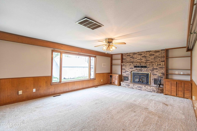 unfurnished living room with a ceiling fan, wainscoting, wood walls, and visible vents