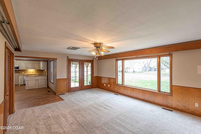 unfurnished living room with a ceiling fan, visible vents, a textured ceiling, and wainscoting