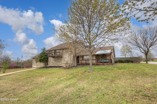 view of front of house featuring a front lawn, fence, a balcony, and stone siding