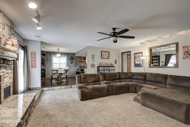 carpeted living area with track lighting, a stone fireplace, ceiling fan, and a textured ceiling