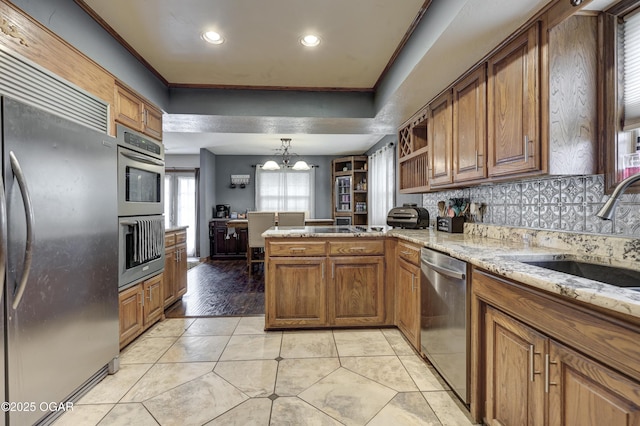 kitchen featuring a peninsula, a sink, appliances with stainless steel finishes, and brown cabinets