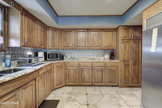 kitchen featuring ornamental molding, appliances with stainless steel finishes, tasteful backsplash, and brown cabinets