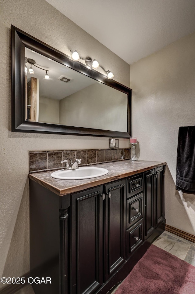 bathroom with a textured wall, baseboards, visible vents, and vanity