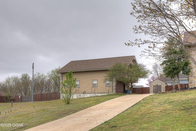 view of property exterior featuring driveway, fence, roof with shingles, and a yard