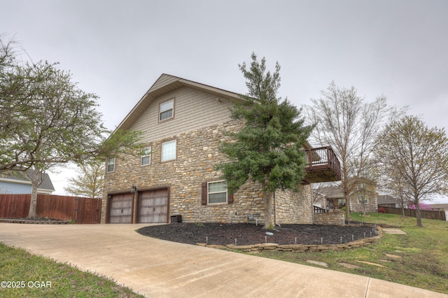 view of property exterior with stone siding, an attached garage, fence, and concrete driveway