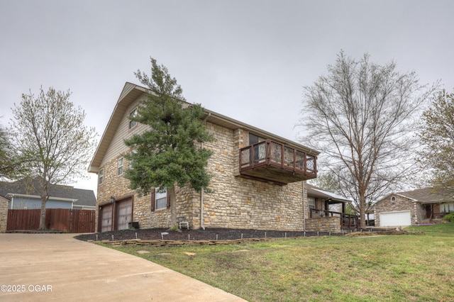 view of side of home featuring stone siding, a balcony, an attached garage, driveway, and a yard