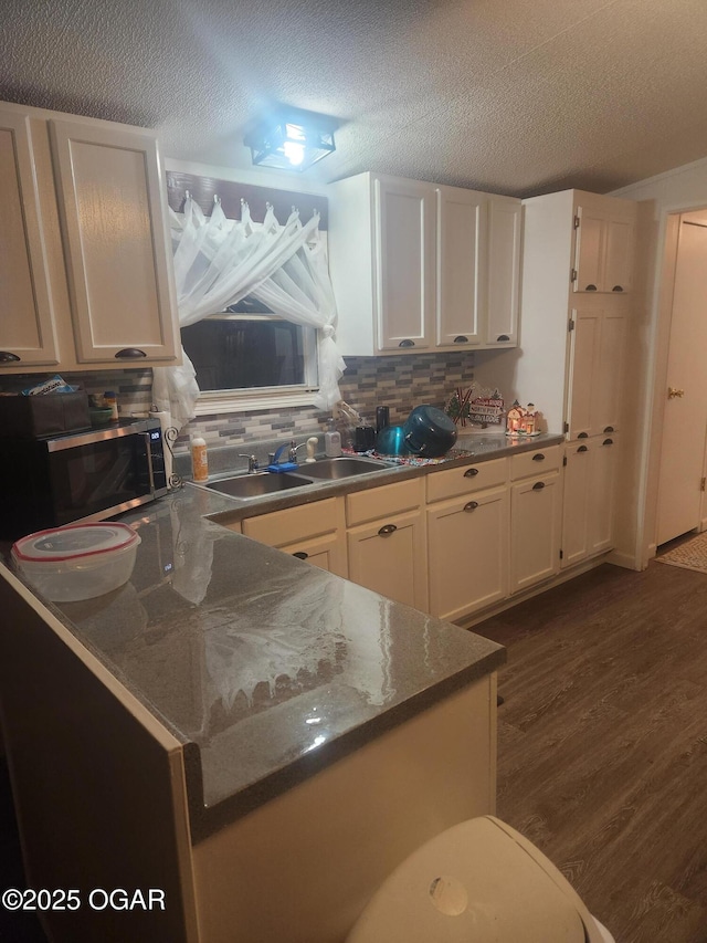 kitchen featuring decorative backsplash, dark wood-style flooring, a textured ceiling, stainless steel microwave, and white cabinetry