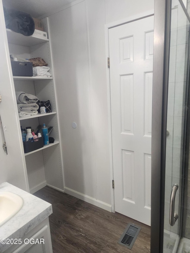 bathroom with visible vents, a shower with door, wood finished floors, and vanity