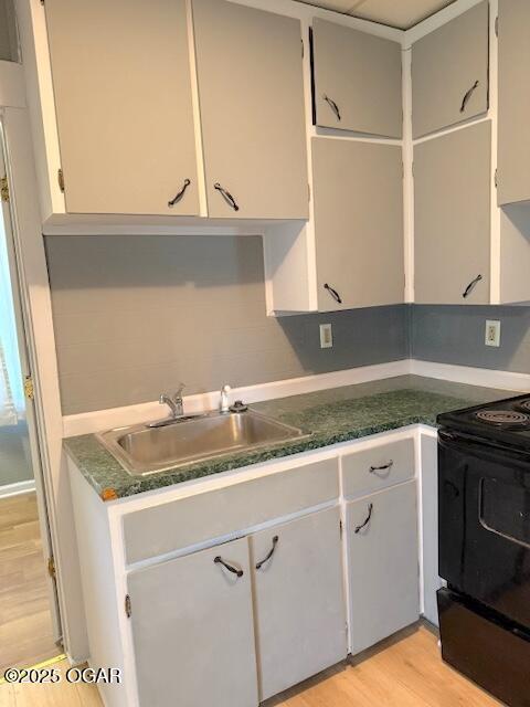 201 N Georgia St, Pittsburg, KS 66762 - kitchen featuring a sink, electric range, light wood-style floors, dark countertops, and white cabinets