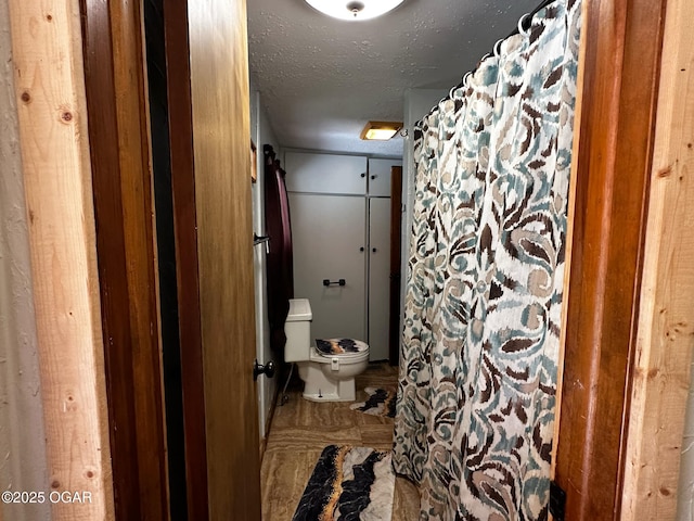 bathroom with toilet, curtained shower, and a textured ceiling
