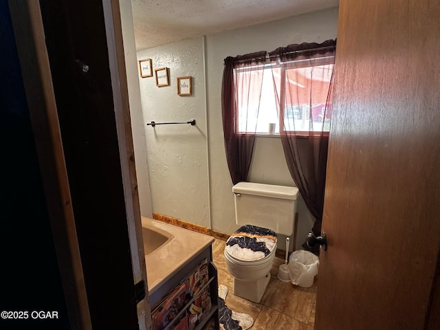 bathroom with toilet, a textured ceiling, a textured wall, and vanity