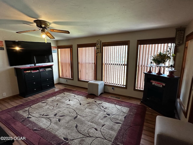 living area featuring visible vents, baseboards, a ceiling fan, and wood finished floors