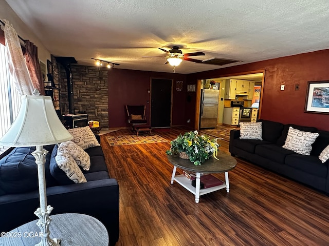 living area featuring a wood stove, ceiling fan, track lighting, a textured ceiling, and wood finished floors