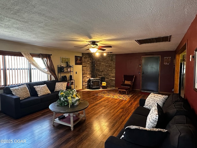 living room with a textured ceiling, a ceiling fan, a wood stove, visible vents, and hardwood / wood-style floors