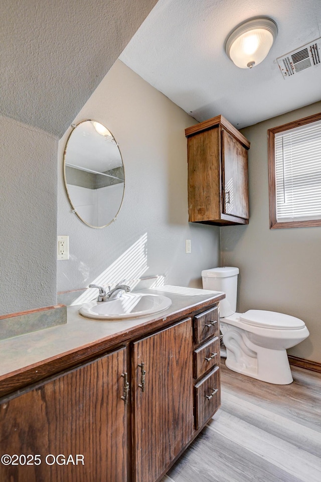 bathroom featuring vanity, a textured ceiling, toilet, visible vents, and wood finished floors