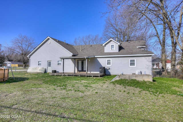 rear view of house featuring fence, a deck, a lawn, and roof with shingles