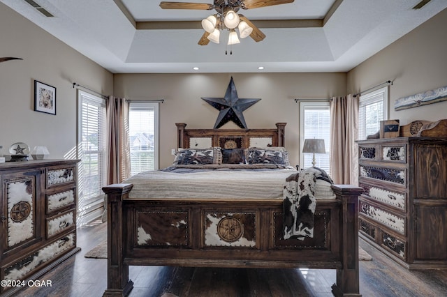 bedroom with a tray ceiling, wood finished floors, ceiling fan, and visible vents