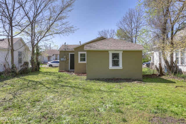 back of house featuring a shingled roof, a lawn, and stucco siding