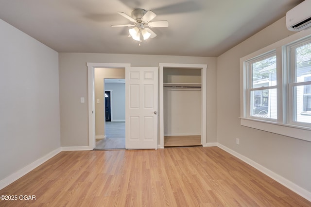 unfurnished bedroom featuring a closet, light wood-style floors, an AC wall unit, and baseboards