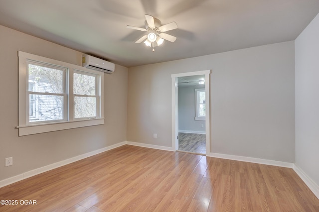 empty room featuring ceiling fan, light wood finished floors, baseboards, and a wall unit AC