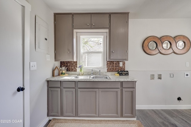 kitchen with electric panel, gray cabinets, light countertops, a sink, and backsplash