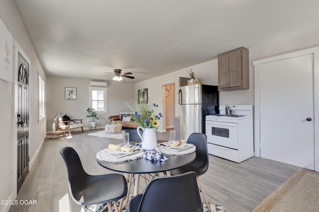dining room with an AC wall unit, light wood-style flooring, a ceiling fan, and baseboards