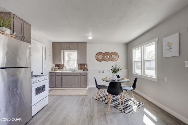 kitchen featuring baseboards, light countertops, freestanding refrigerator, light wood-style flooring, and white gas range oven