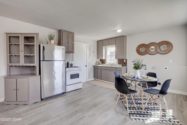 kitchen featuring a sink, light countertops, freestanding refrigerator, light wood-style floors, and white gas range