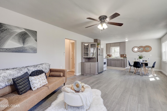 living area featuring light wood-type flooring, baseboards, and ceiling fan