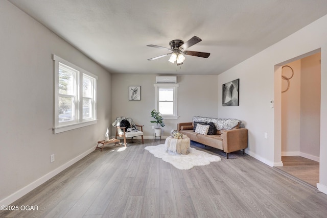 living area with ceiling fan, an AC wall unit, baseboards, and wood finished floors