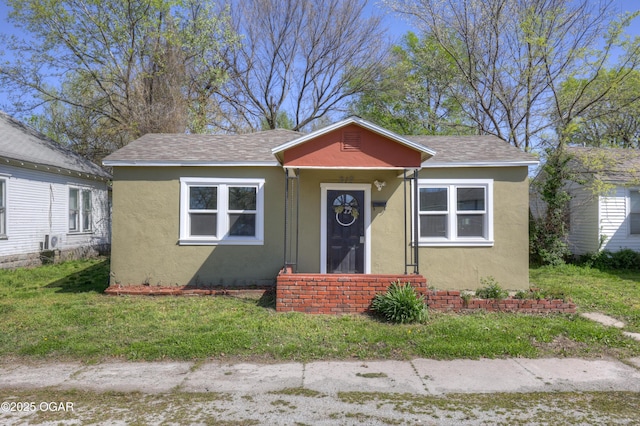 bungalow-style home featuring roof with shingles, stucco siding, and a front yard